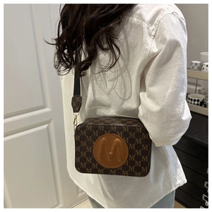 Woman wearing a brown monogram crossbody camera bag with wide strap and M logo