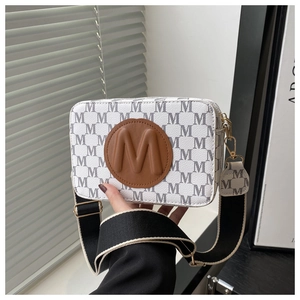 Détail d'un sac bandoulière blanc avec monogramme M gris et écusson en cuir marron