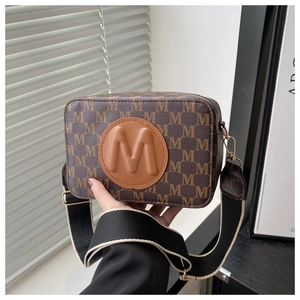 Gros plan du sac caméra marron avec imprimés M et large bandoulière en toile bicolore