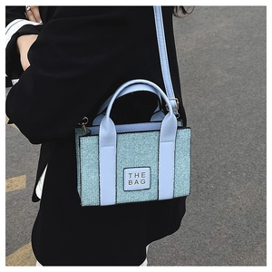 Light blue woven tote bag with adjustable strap shown from a stylish side street view