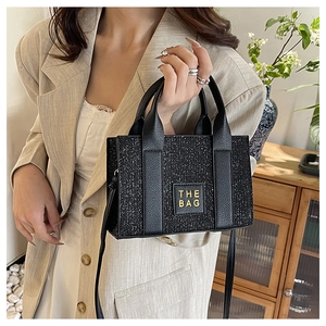 Detail of black sequined tote bag featuring THE BAG leather patch and crossbody strap