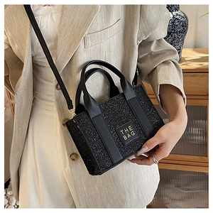 Detail view of mini black sequin tote bag with THE BAG leather patch and top handles