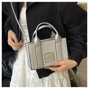 Close-up of silver sequin mini tote bag with short handles and THE BAG text on patch