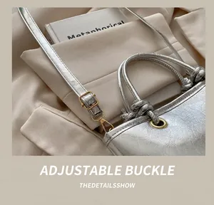 Detail of golden adjustable metal buckle and strap on silver wrinkled texture bucket bag