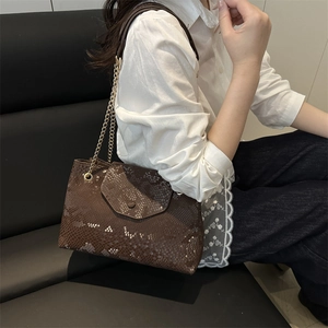 Brown snake skin shoulder bag with gold chain strap carried by a woman in a white shirt