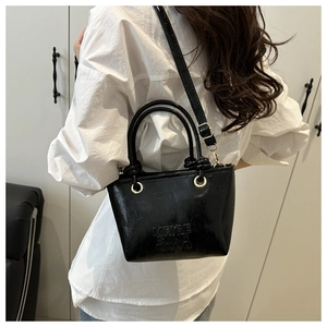 Detail of black glossy bucket bag with embossed letters and adjustable crossbody strap