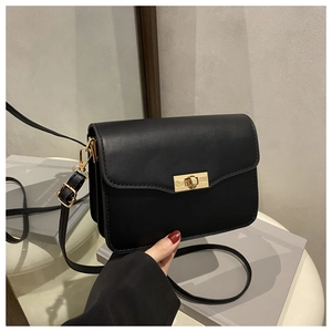 Close-up of minimalist black square bag featuring a gold rotating lock and smooth leather