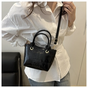 Chic black mini bucket bag with embossed lettering and golden hardware on a model
