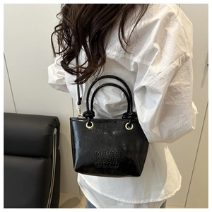 Close-up of black glossy patent leather crossbody bag with metallic rings and embossed letters
