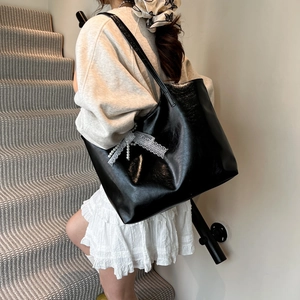 Minimalist black tote bag with lace pearl bow decoration shown on shoulder in daily use