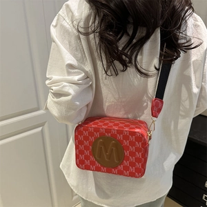 Petit sac à bandoulière rouge avec motif M et sangle réglable porté par un mannequin