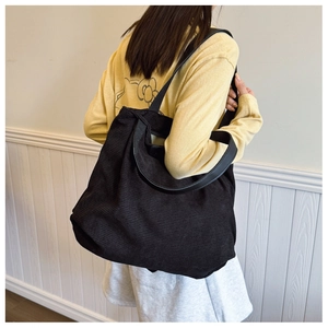 Detailed view of a black corduroy tote bag worn by a model against a white wall