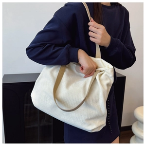 Detail of white corduroy tote bag with wide brown strap and leather logo patch