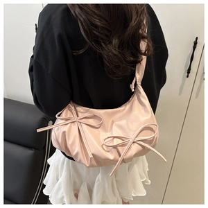 Detail of pink crescent bag with bow accents worn by a model in a minimalist setting
