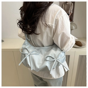 Detail of light blue bow shoulder bag with glossy texture worn by a model in a cozy setting