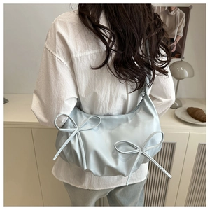 Detail of light blue crescent bag featuring dual bow accents and pleated strap texture