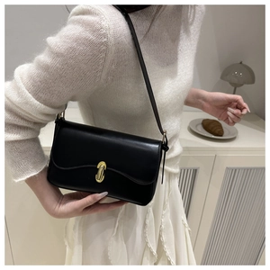 Detail of black leather underarm bag featuring a prominent gold capsule metal buckle