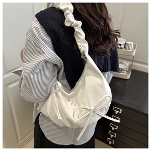 Detail of white pleated cloud bag featuring ribbon bow and ruffled shoulder strap