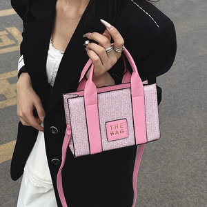 Pink sparkly tote bag with THE BAG lettering and adjustable crossbody strap on model