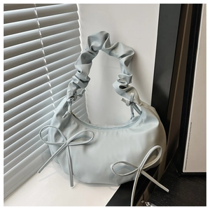 Detail of light blue crescent bag featuring ruffled handle and delicate bow accents