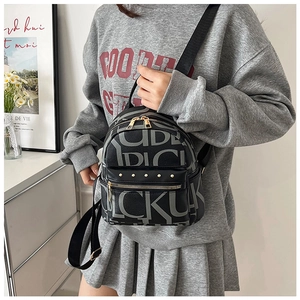 Detail of artistic grey lettering on black PU leather backpack with gold metal zippers