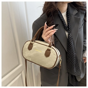 Detail of canvas cylinder bag with brown leather trim and golden hardware buckle
