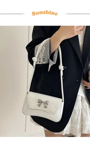Detail of white leather shoulder bag featuring woven texture and silver metal bow buckle