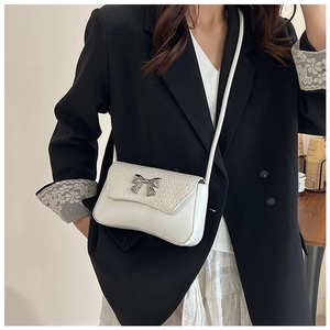 Detail of white PU leather crossbody bag featuring a silver bow buckle and woven texture