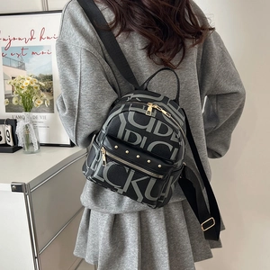 Fashionable black backpack with letter print and gold studs worn by a model