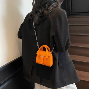 Petit sac à main orange tendance avec bandoulière chaîne argentée porté par un mannequin