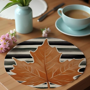 Detail of round linen placemat with maple leaf print and black white stripes on wood table