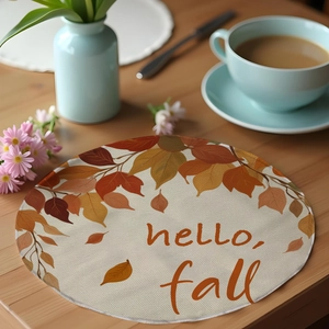 Close-up of linen place mat with autumn leaf pattern and 'hello fall' text on wooden table