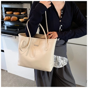 Detail of minimalist cream-white tote bag with litchi texture and metal logo plate