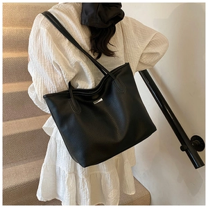 Dettaglio della borsa tote in pelle martellata nera con logo e vestito bianco