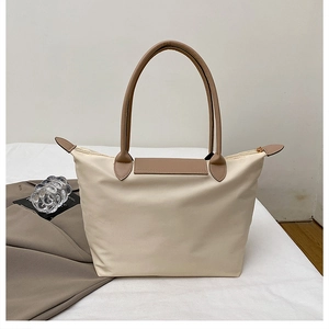 Détail du rabat en cuir marron et de la fermeture éclair dorée sur le sac en nylon beige
