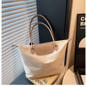 Gros plan du sac cabas en nylon beige avec poignées et rabat en cuir sur un livre