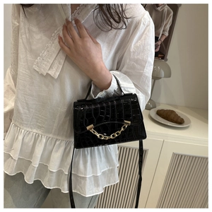 Detail of black crocodile texture handbag featuring decorative gold chain and leather handle