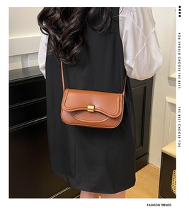 Brown leather shoulder bag featuring wave-edged flap and golden metallic square buckle
