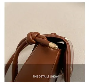 Close-up of knot-designed cylindrical strap and golden metal clasp on brown leather bag