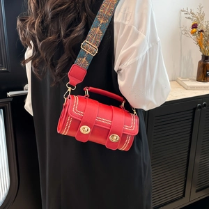 Red cylindrical handbag with ethnic pattern strap shown in a minimalist room setting