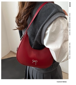 Close-up of a red leather crescent bag with a silver bow metal decoration on a model