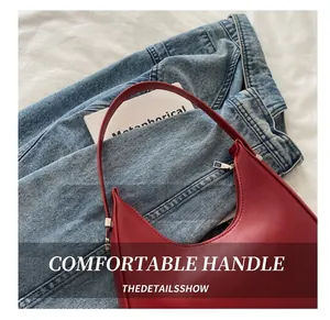 Détail du sac sous l'aisselle en cuir rouge avec bandoulière fine sur fond denim