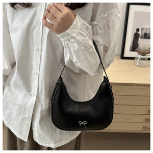 Close-up of black hobo bag with silver bow detail worn by model in white blouse