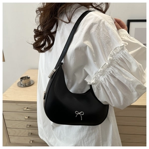 Detail of a matte black moon crescent shoulder bag featuring a silver bow metal charm