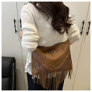 Detail of vintage brown fringe bag with metal rivets and crossbody strap shown on model