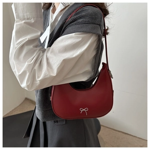 Detail of red crescent shoulder bag with silver bow buckle on model's outfit