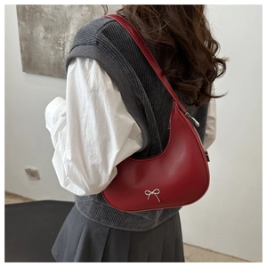 Red crescent shoulder bag with silver bow detail styled on a neutral outfit