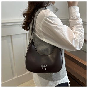 Detailed shot of dark brown crescent shoulder bag featuring a silver metal bow accessory
