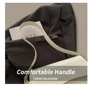Close-up of white flap shoulder bag with gold metal hardware on dark grey suit