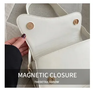 Macro shot of gold magnetic clasp and asymmetric flap on white crossbody saddle bag